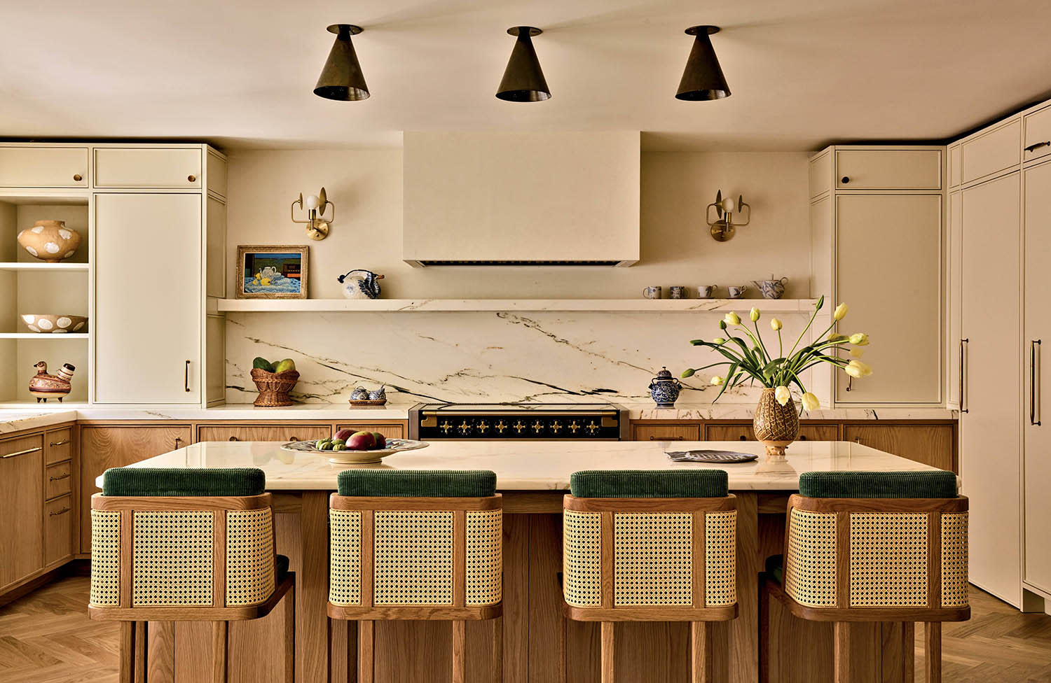 Four chairs sit at a kitchen island with a marble countertop and a trio of lights hanging overhead.