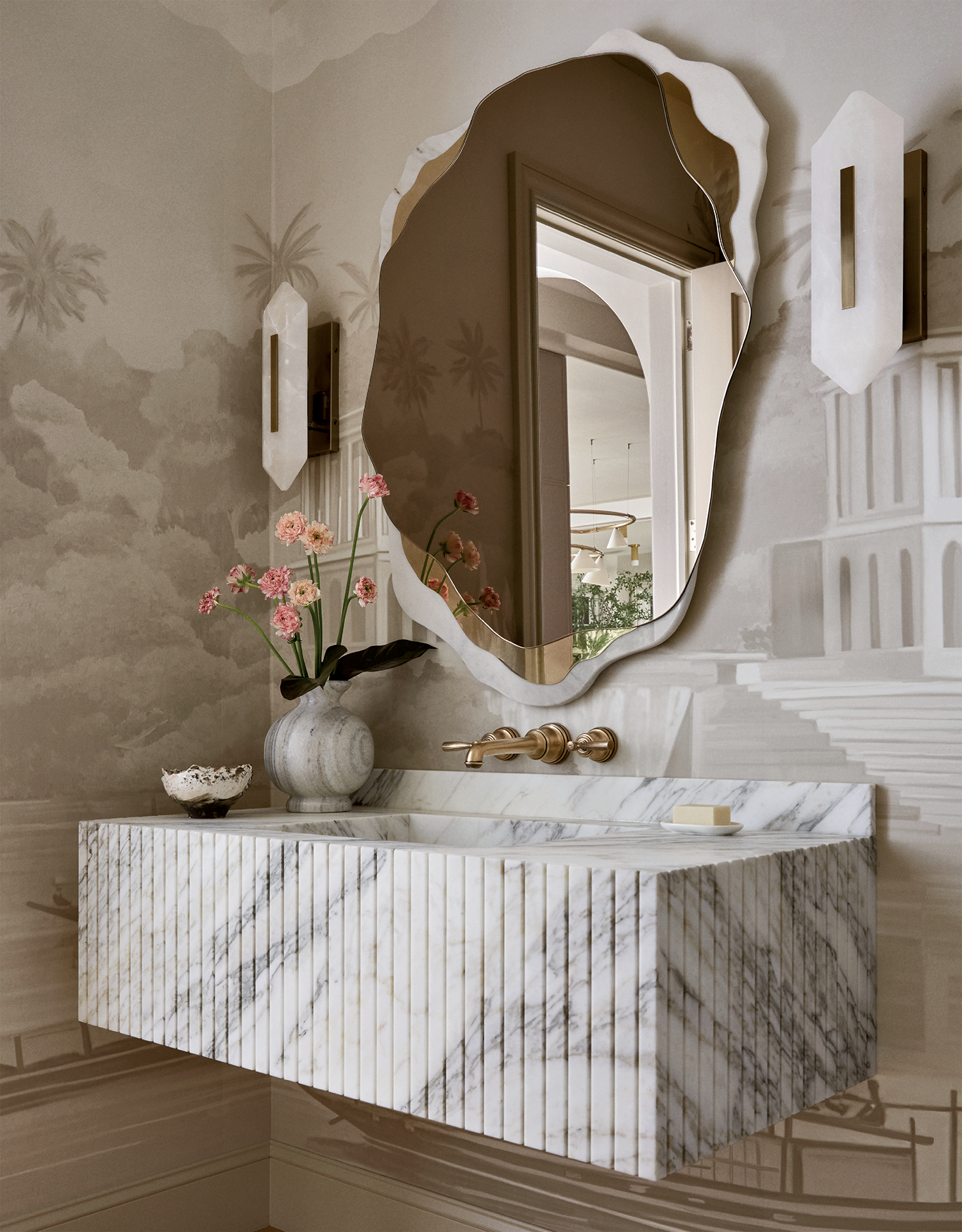 A bathroom with an angular mirror and marble sink flanked by sconces.