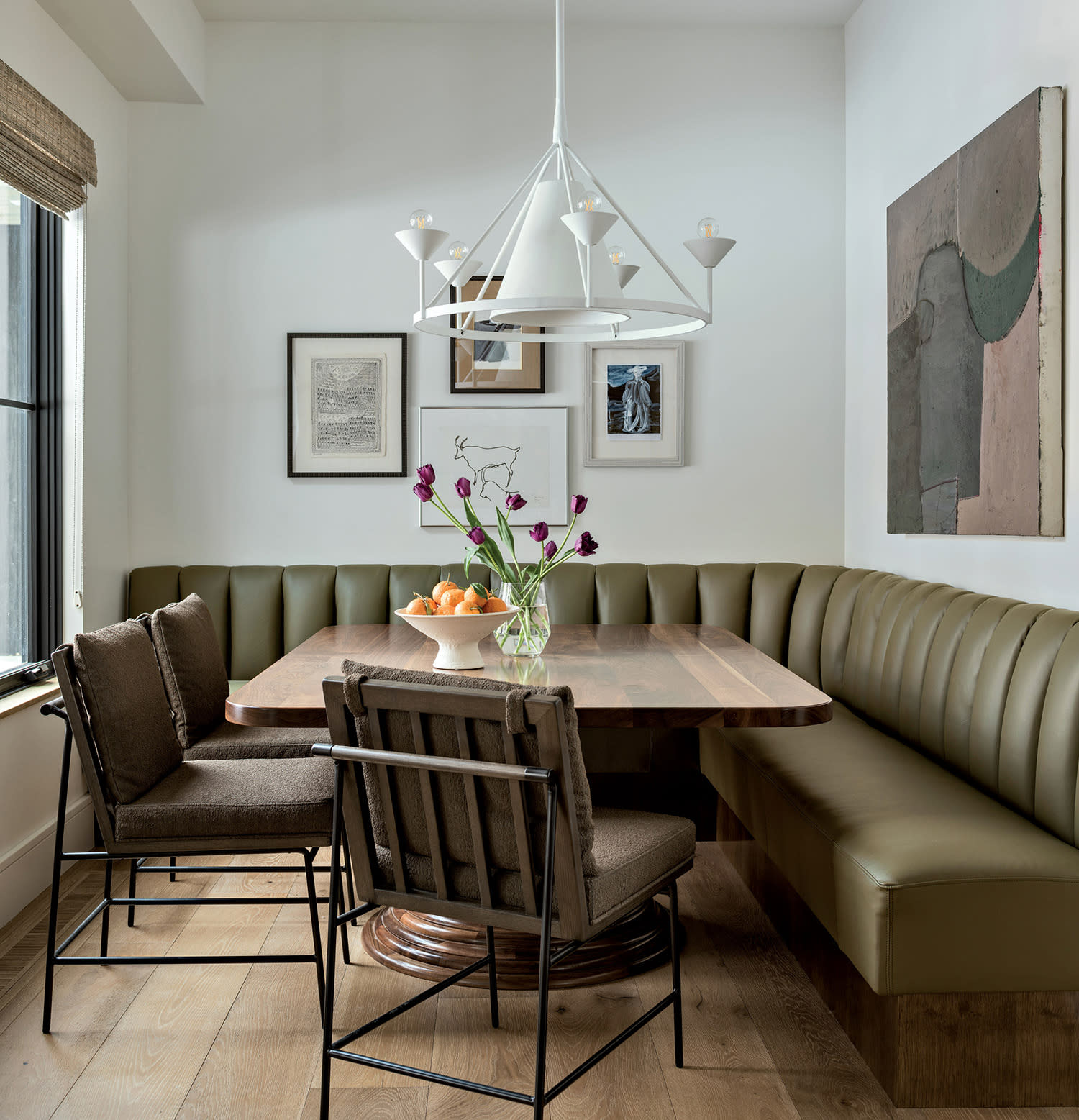 A cozy dining nook with an olive-green leather bench and two brown cushioned chairs around a wooden table.