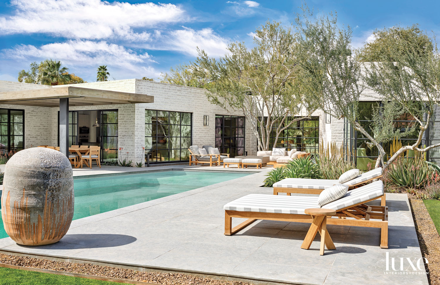 A poolside patio with gray-and-white chaise lounges. In the background is a seating area.