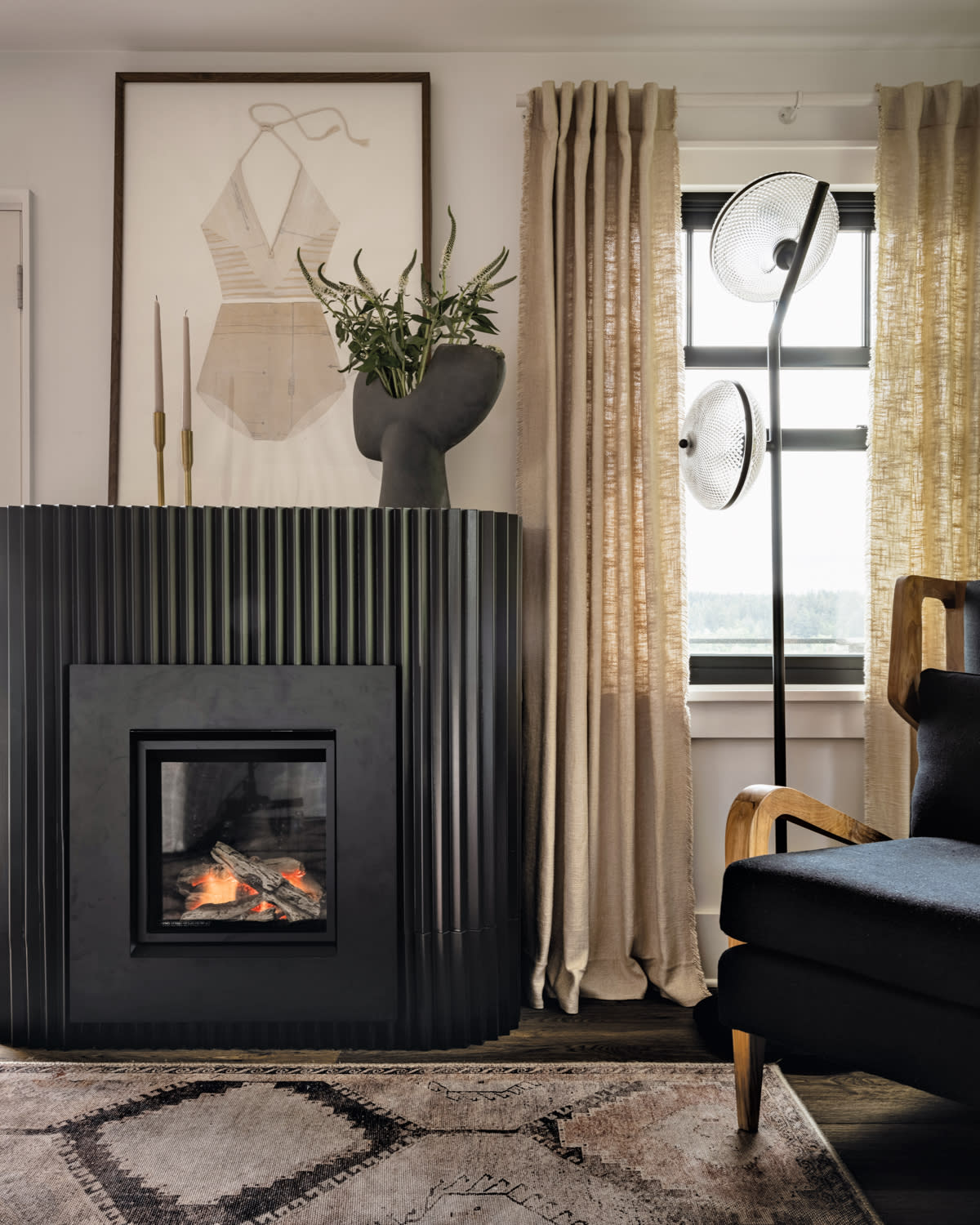 Fireplace with fluted black surround topped next to a window with cream-colored drapes