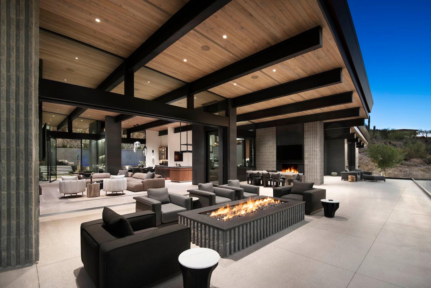Luxurious modern patio with a wooden ceiling, plush seating, and a rectangular fire pit table. Open space evokes warmth and sophistication under twilight sky.