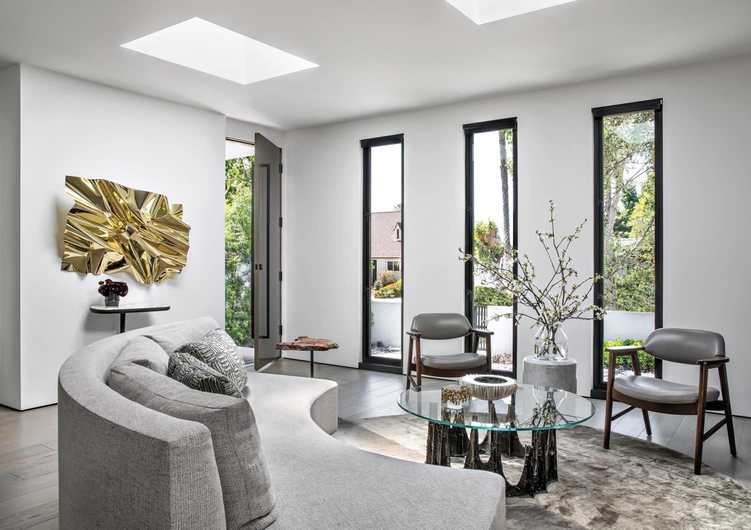 Brutalist living room with slit windows, a gray couch, glass coffee table and gold wall sculpture