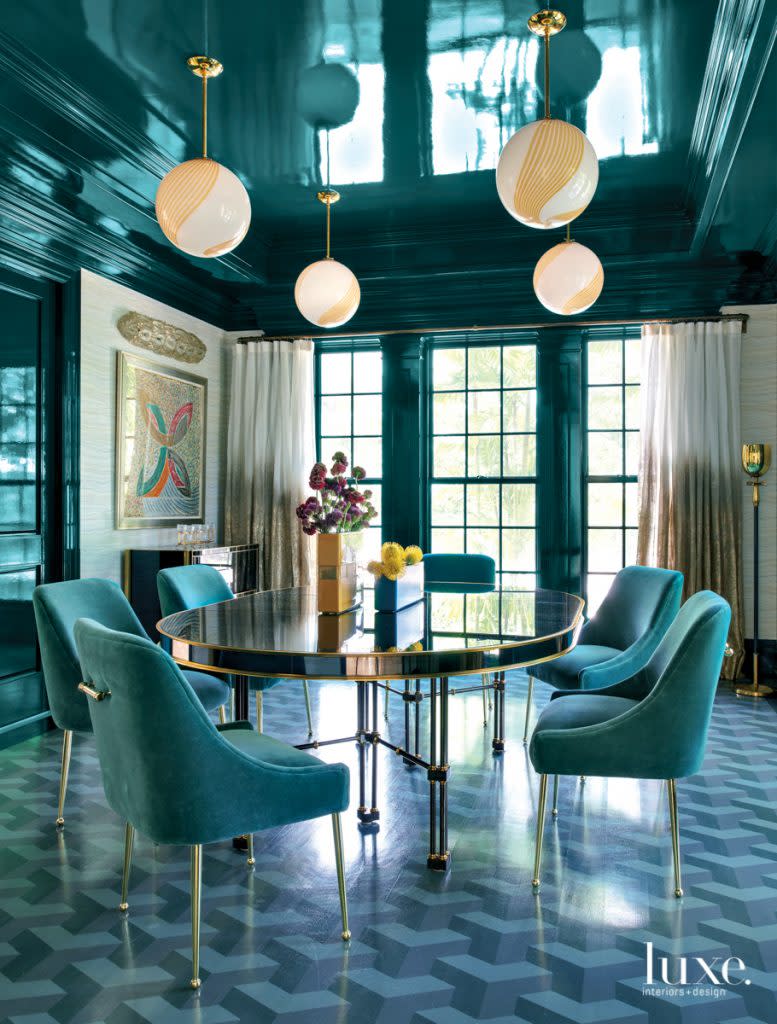 Rafferty carried the high-gloss effect into the dining room with Benjamin Moore's Pacific Sea Teal and a custom painted floor. Midcentury pendants hang above a 1940s Maison Jansen table and Anthropologie chairs. Frank Stella artwork is displayed against Thibaut's Treviso Marble wallpaper. A vintage Tommi Parzinger floor lamp stands by draperies made of a Carolyn Ray material.