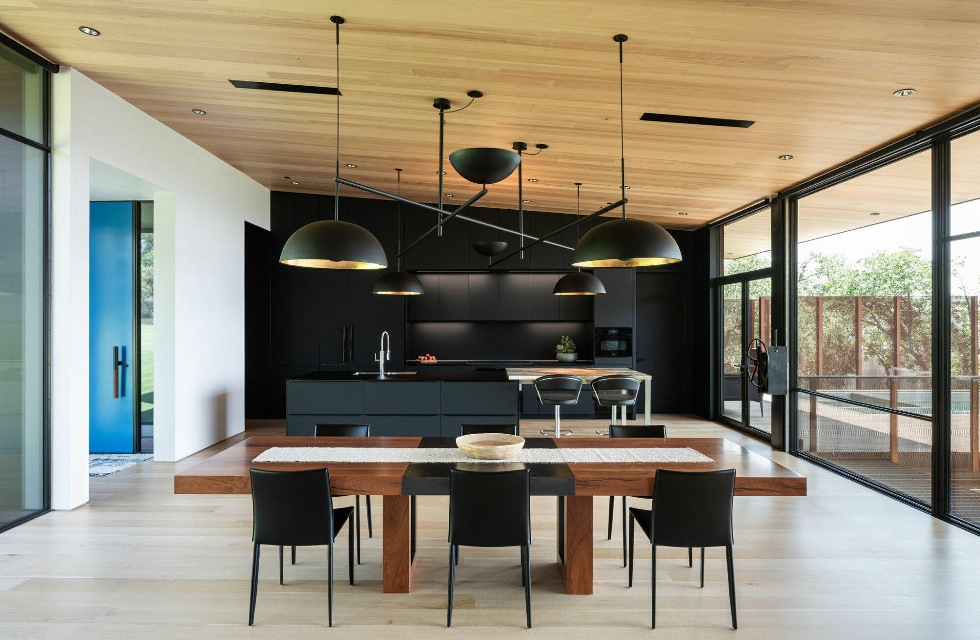 A contemporary kitchen and dining room with sleek wooden floors and walls painted in a stylish black hue.