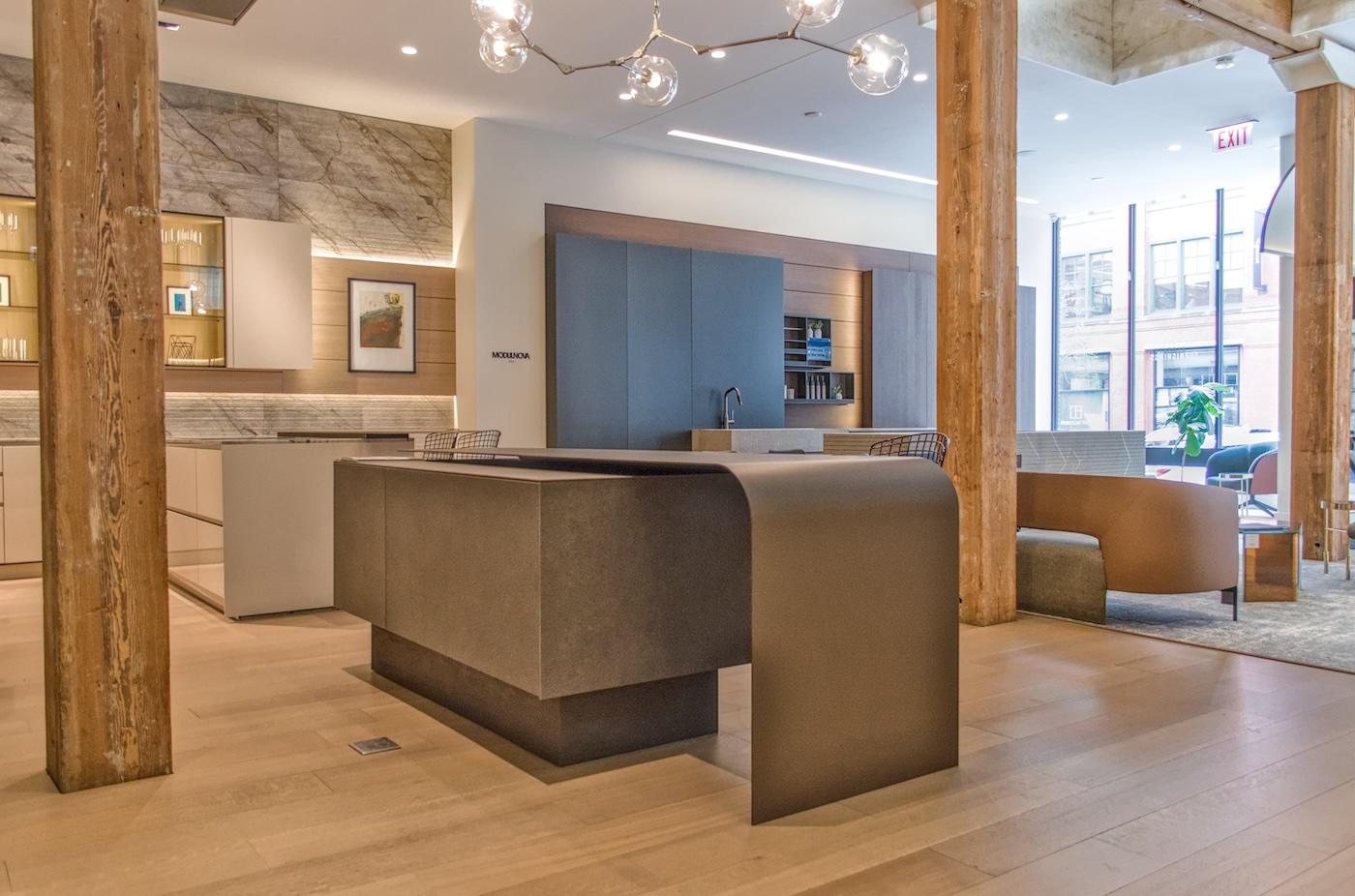 Modern kitchen showroom with wooden beams, sleek stone countertops, and a minimalist design. Natural light illuminates the airy, sophisticated space.