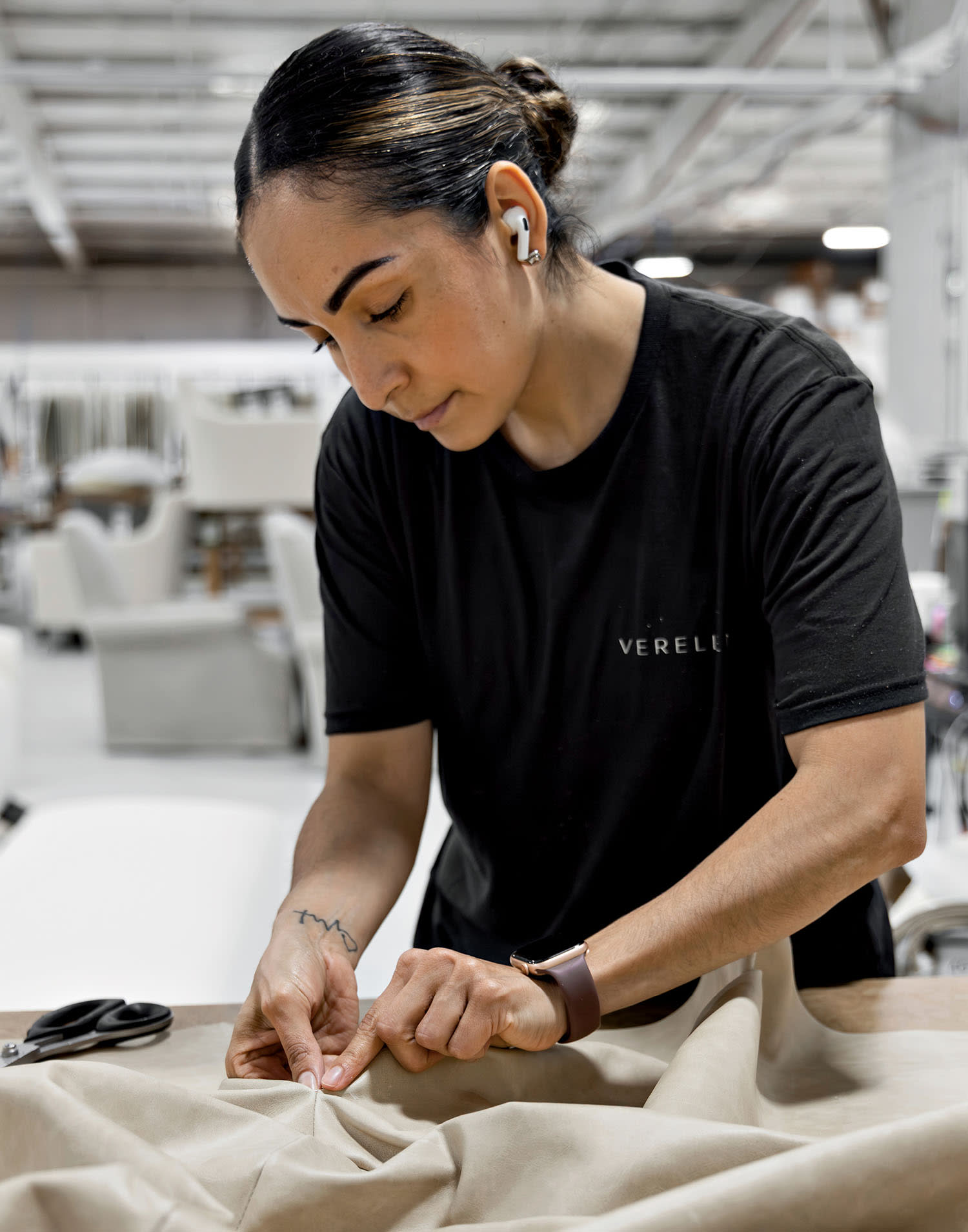 A woman with her hair up and headphones in her ears works on fabric in the Verellen showroom.