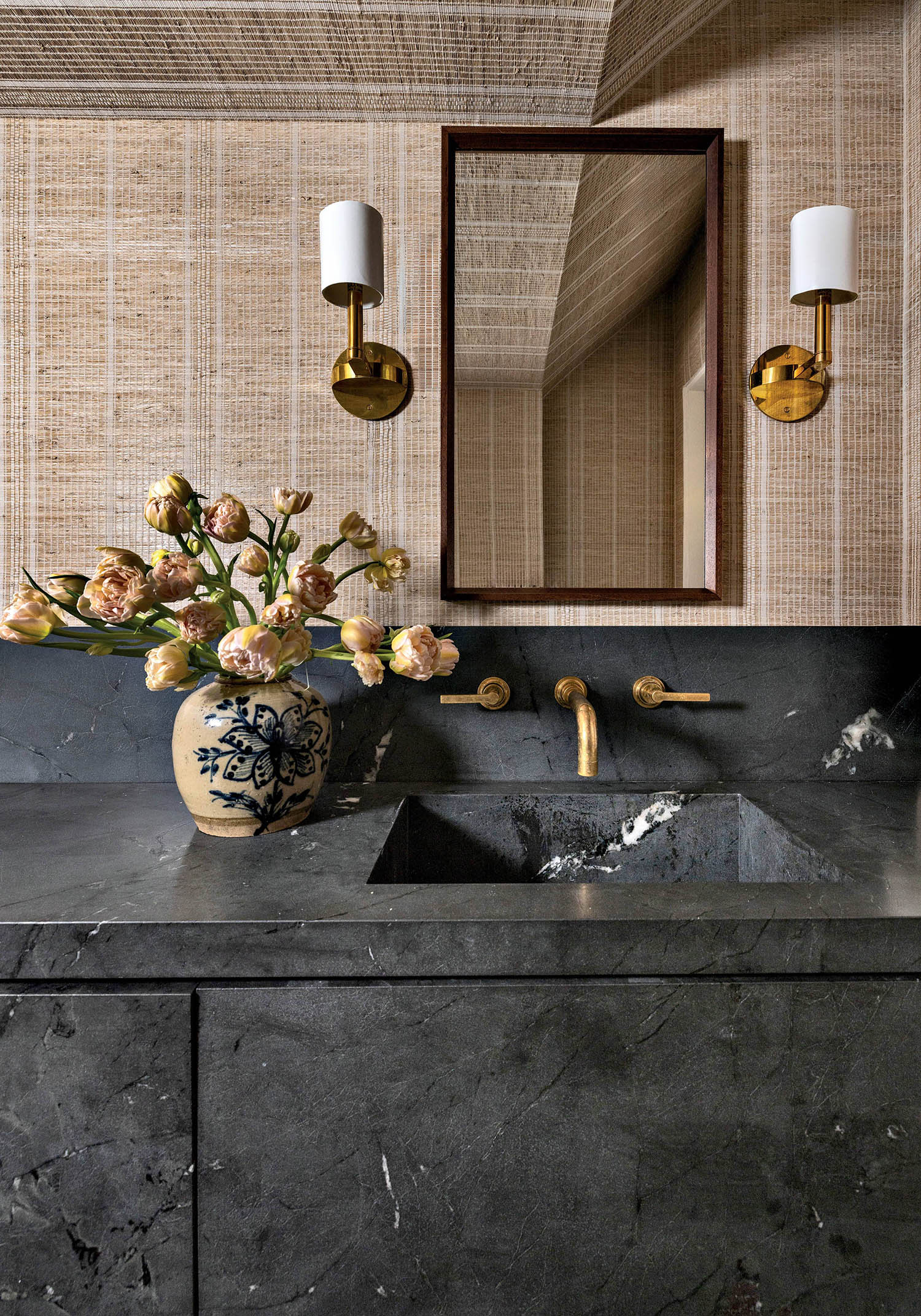 A bathroom vanity with a sink, mirror and paneled wallcovering holding sconces between a mirror.