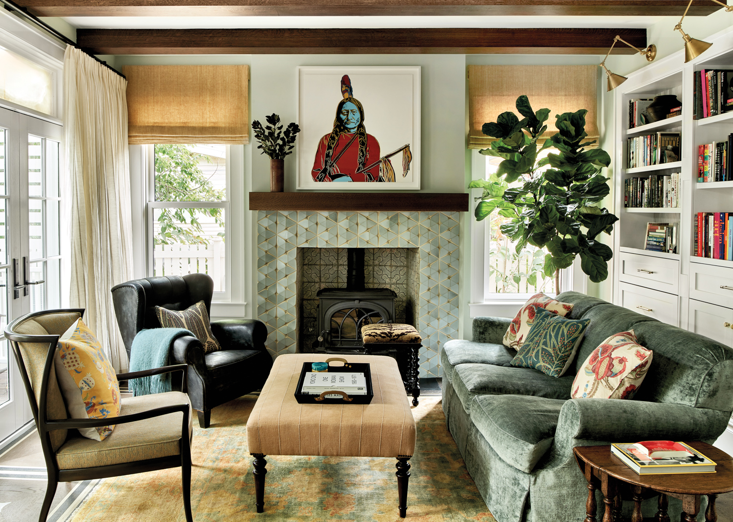 Family room with tile-lined fireplace, contemporary artwork, a velvet lined sofa and two armchairs, plus white bookshelves by Onyx & Oak