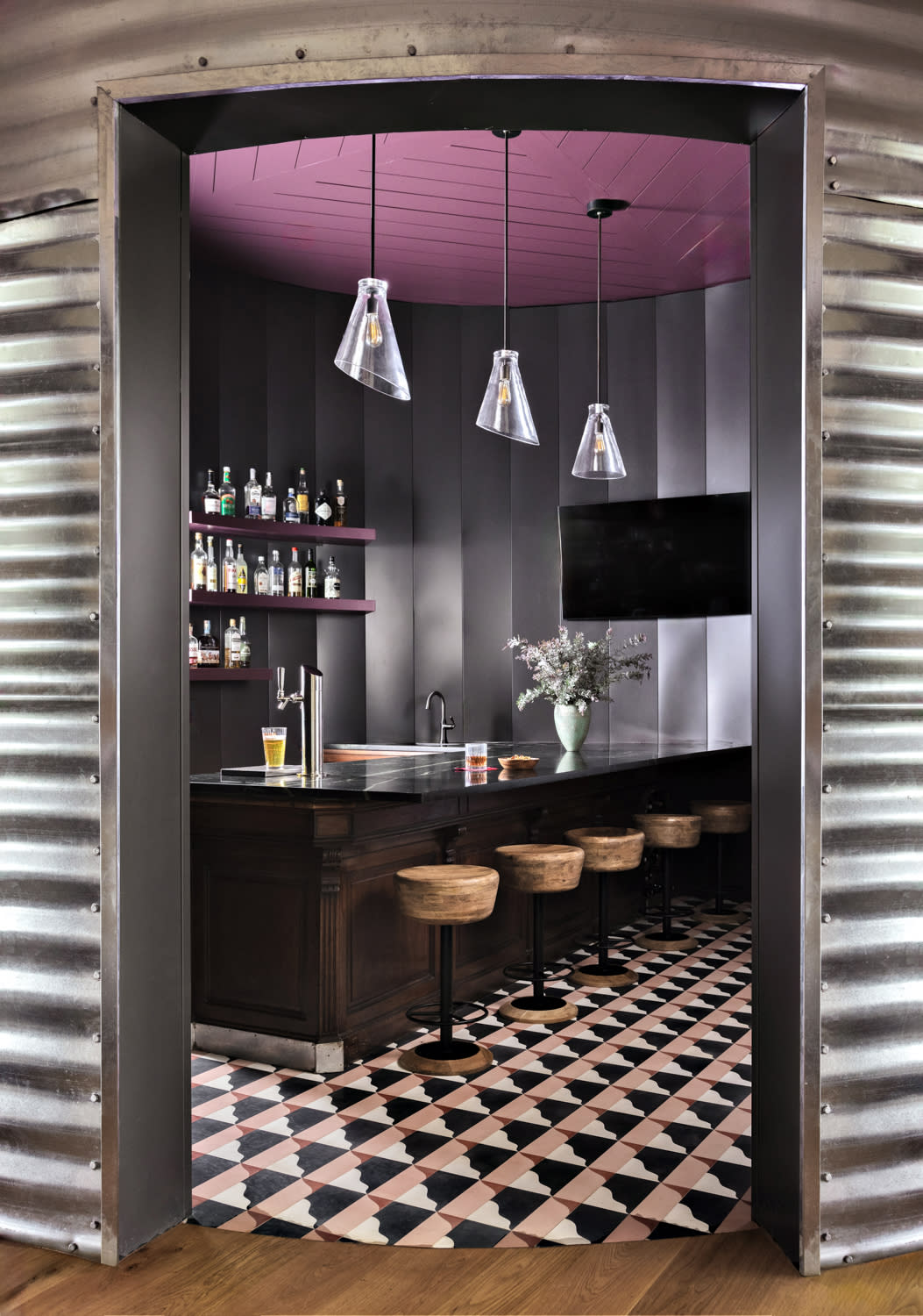 Cozy modern bar with wooden stools, geometric floor tiles, and pendant lights.