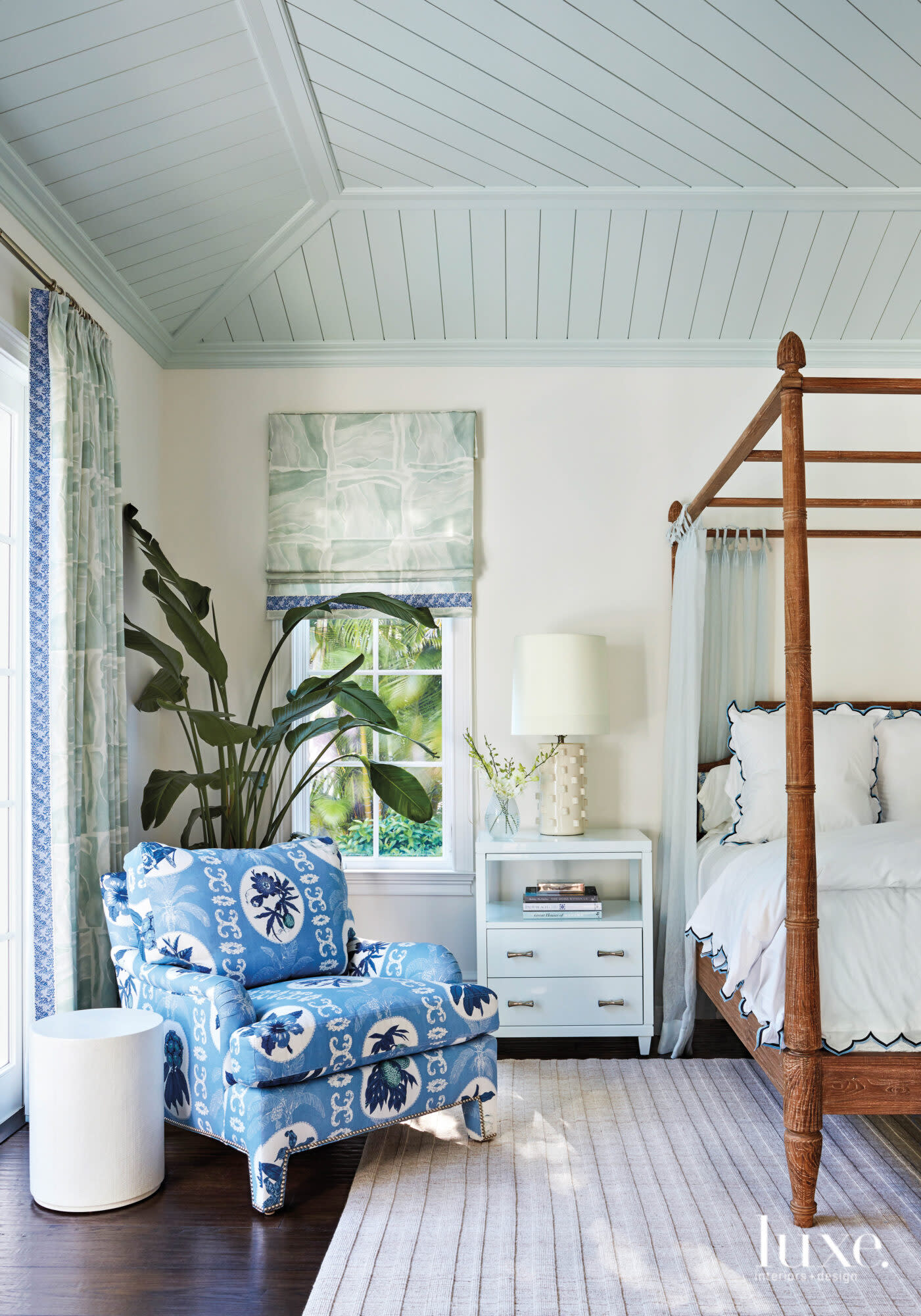 Bedroom with blue armchair and wood canopy bed.
