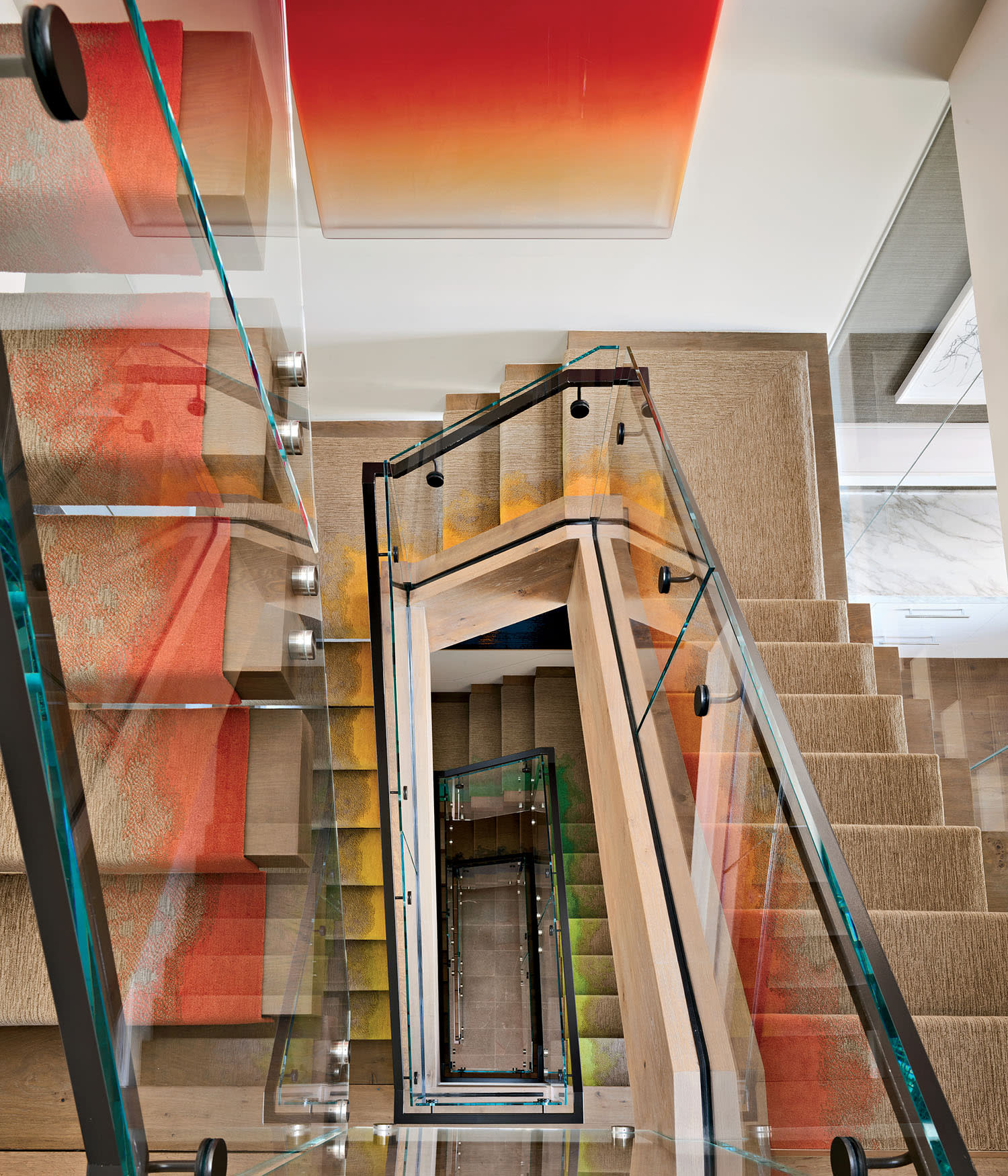 Spiral staircase with glass rails, viewed from above, surrounded by vibrant orange and red abstract art, creating a modern and dynamic feel.