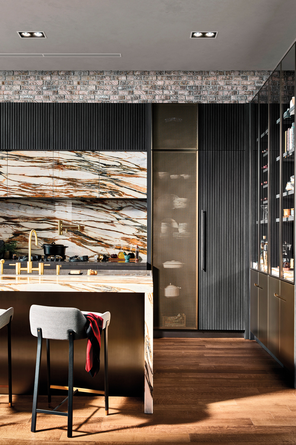 A kitchen on display in a showroom with a gold-veined marble backsplash and matching island, with gray bar stools.