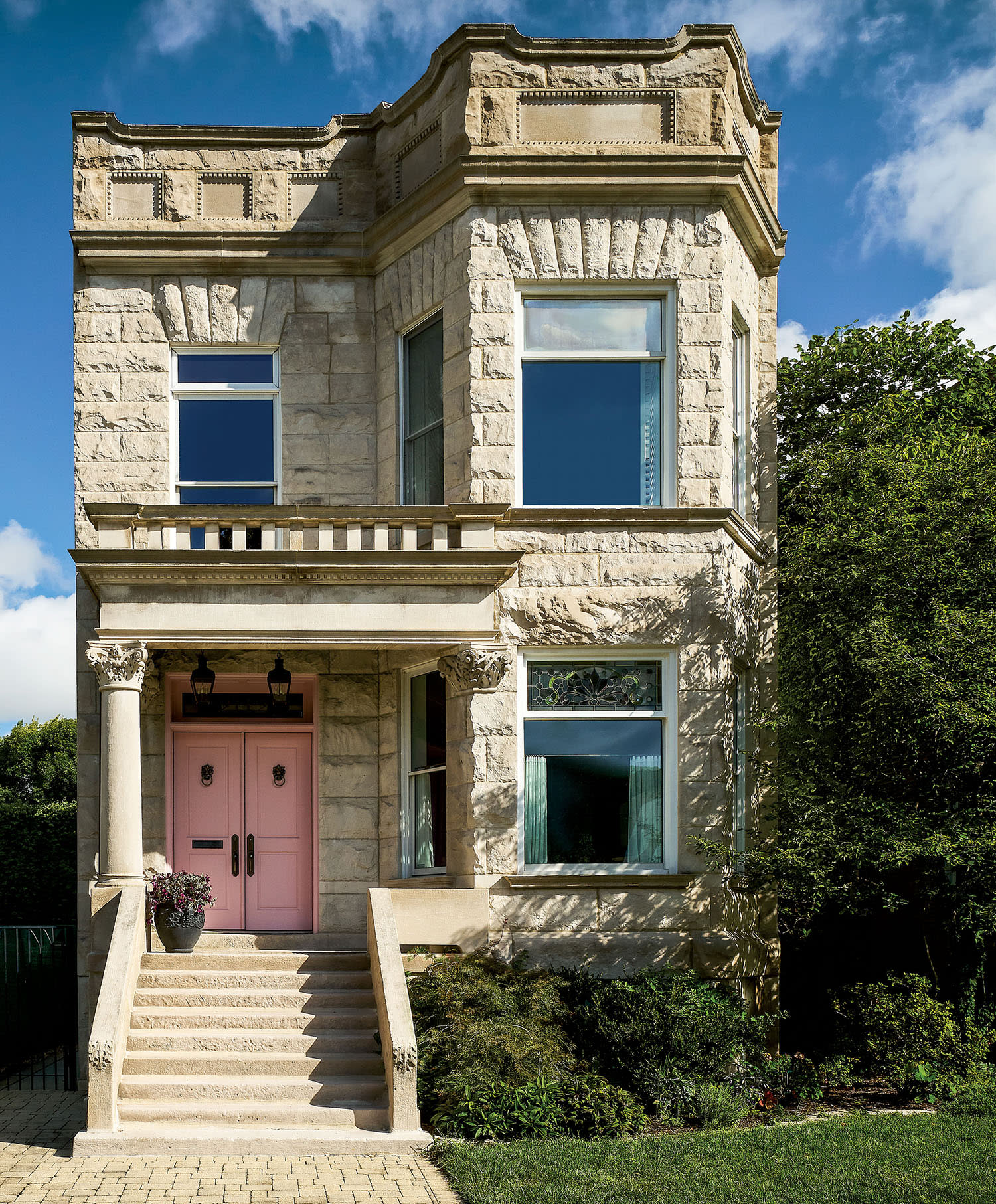 The exterior of a greystone home with large windows and a staircase leading to a bright pink door.