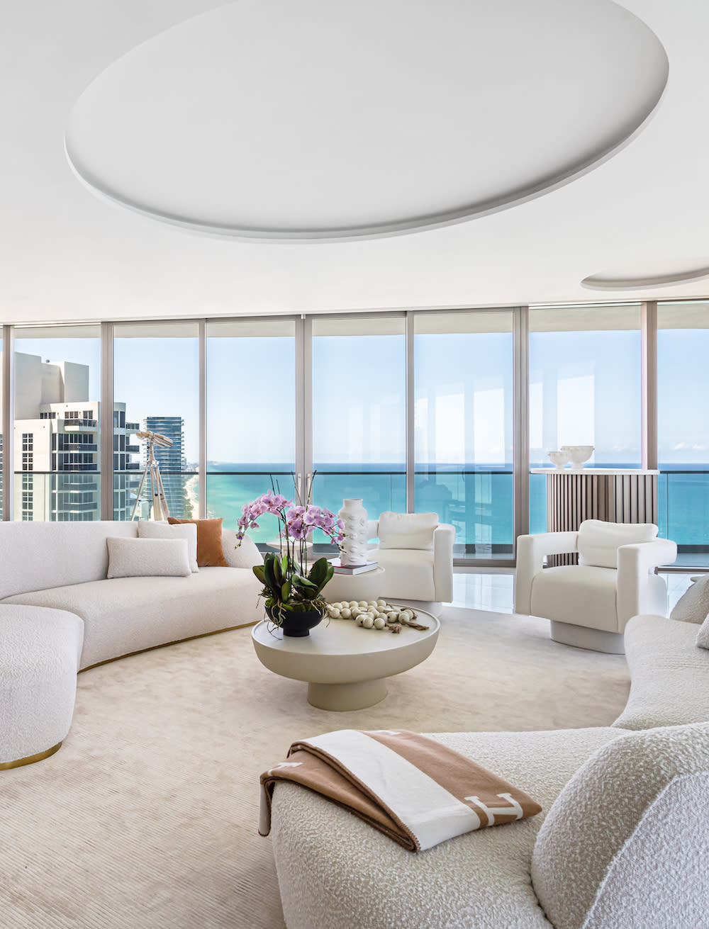 Stylish living room with white furnishings, offering a breathtaking view of the ocean through expansive glass doors.