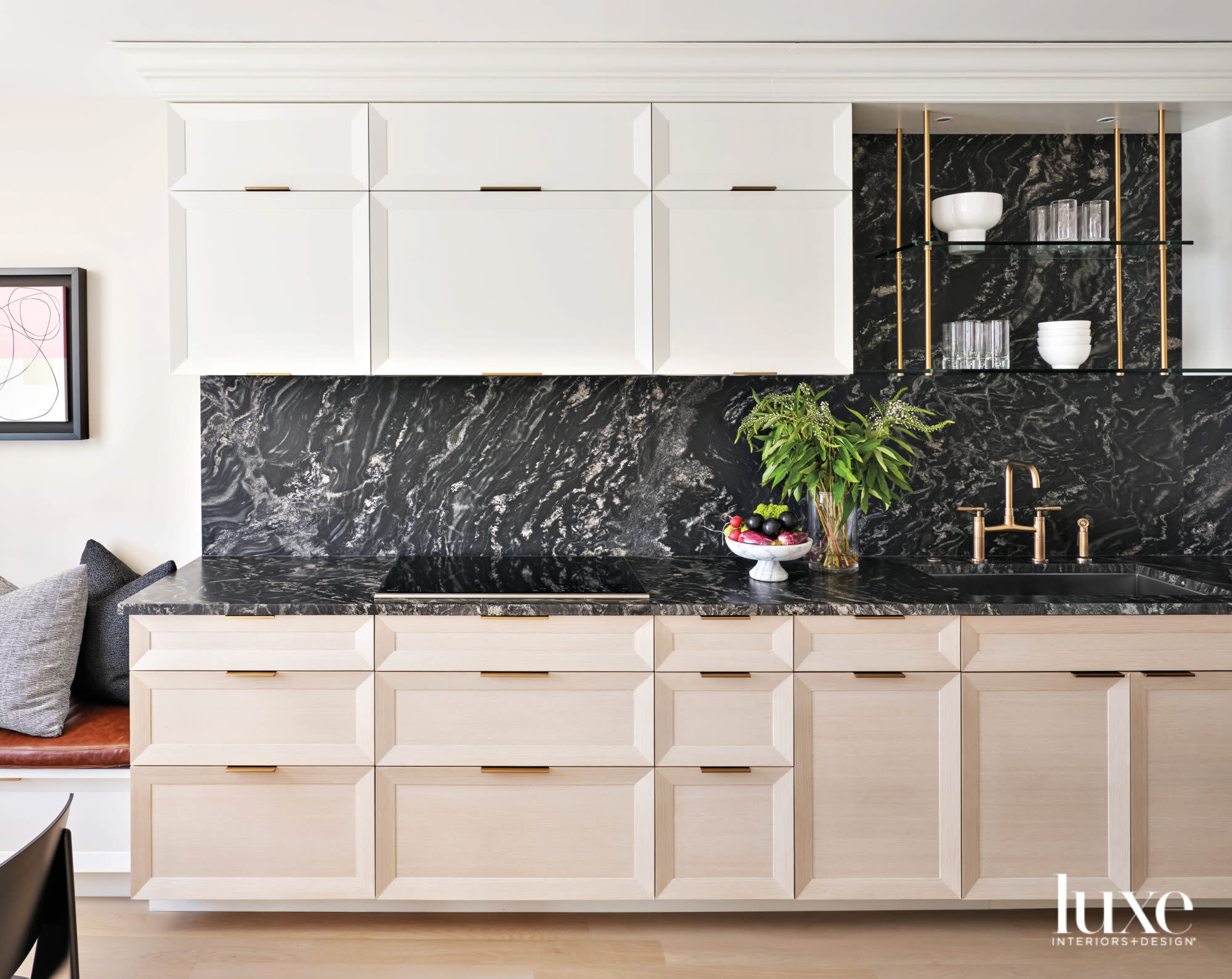 A kitchen with black marble countertops, light oak bottom cabinetry and white upper cabinetry.