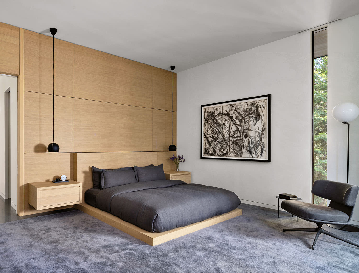 Modern bedroom with a minimalist design. Features a wooden accent wall, low gray bed, and sleek chair. 