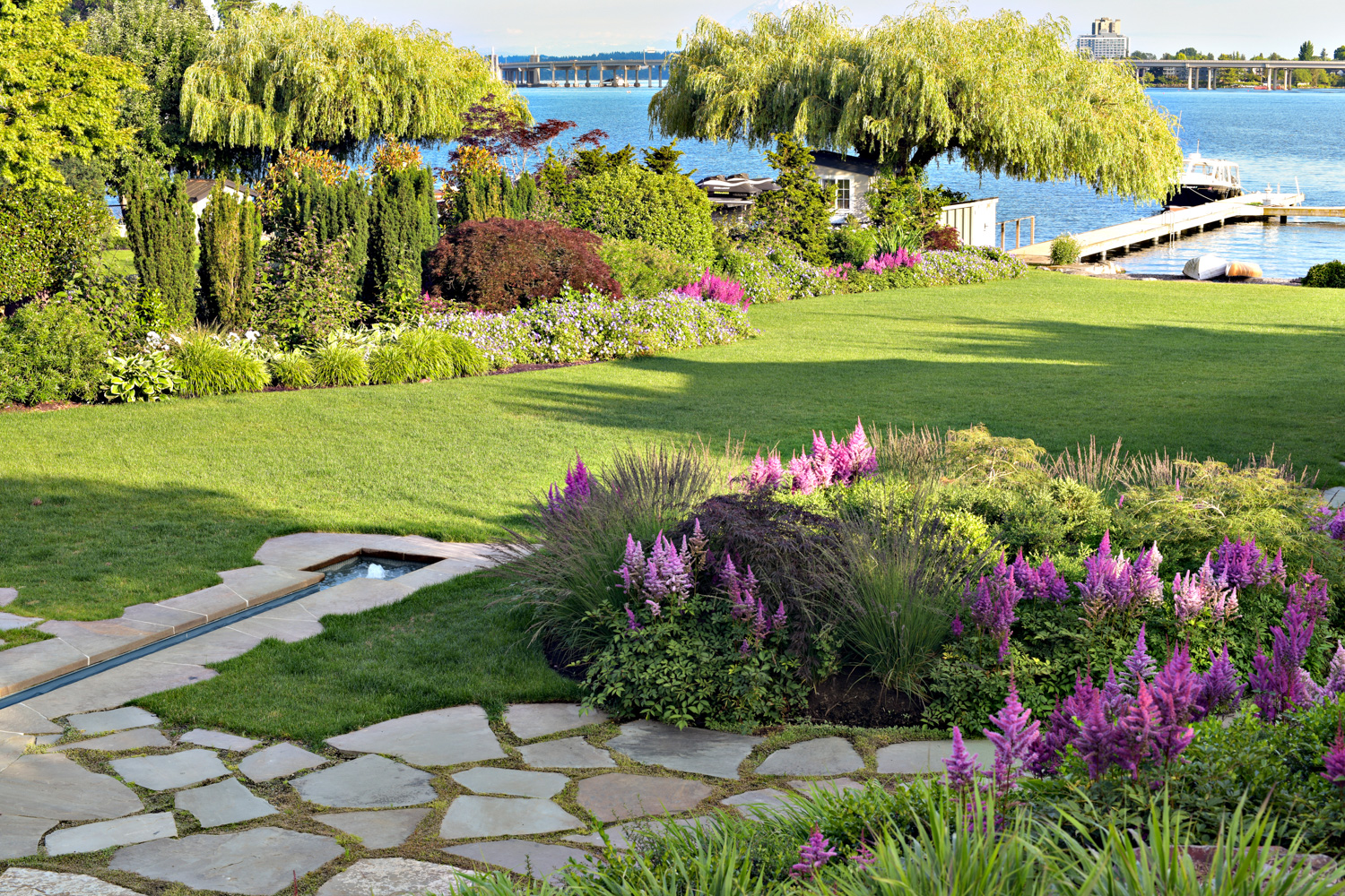 a sweeping lawn with bright plants and views of the lake beyond