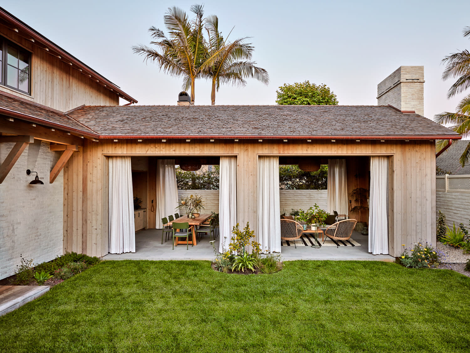 A backyard featuring a patio and a covered patio, surrounded by greenery and outdoor furniture.