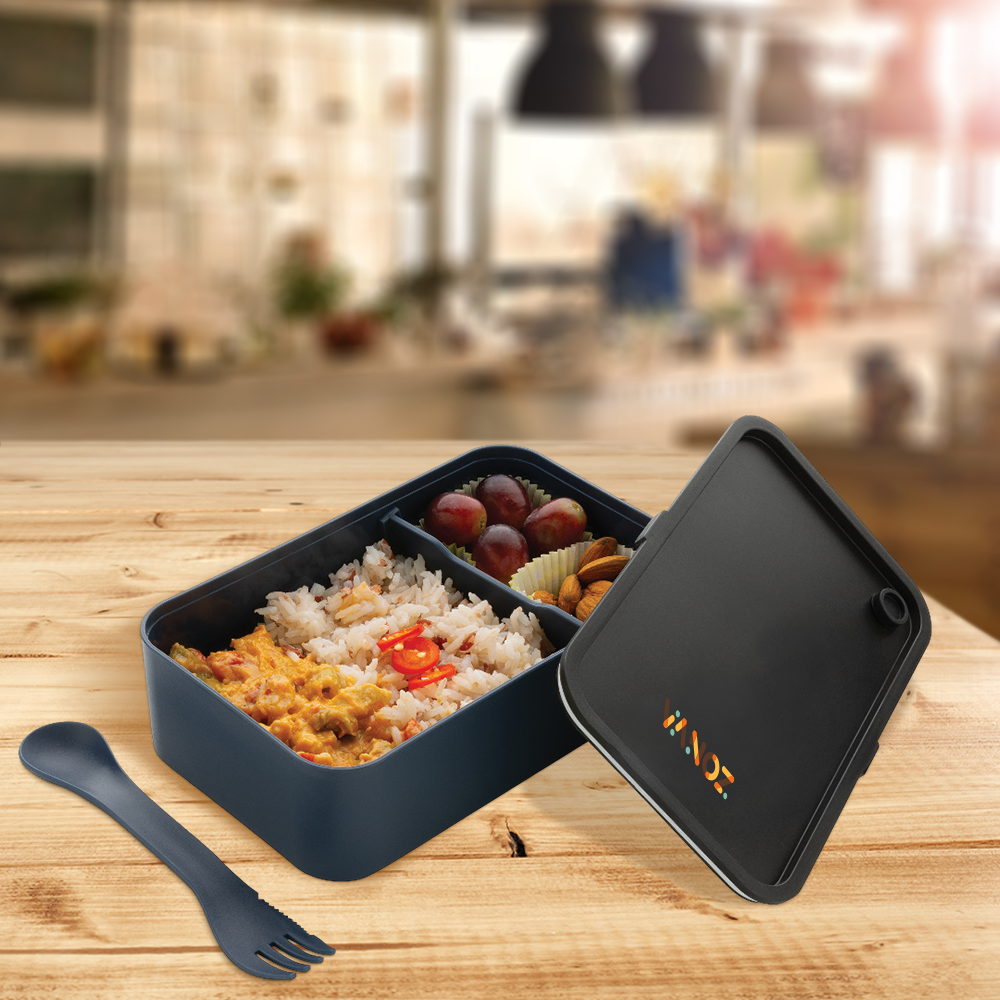Open navy GRS lunch box filled with rice and vegetables beside its spork
