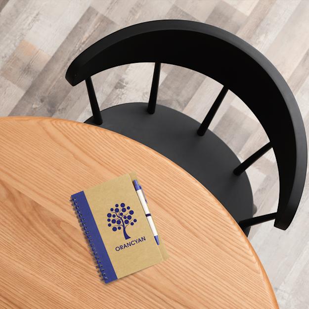 Recycled notebook with tree logo on a wooden table beside a black chair