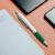 Stylo Nash deluxe blanc avec impression de logo multicolore et grip vert posé sur un carnet à spirale ouvert à côté d'un téléphone
