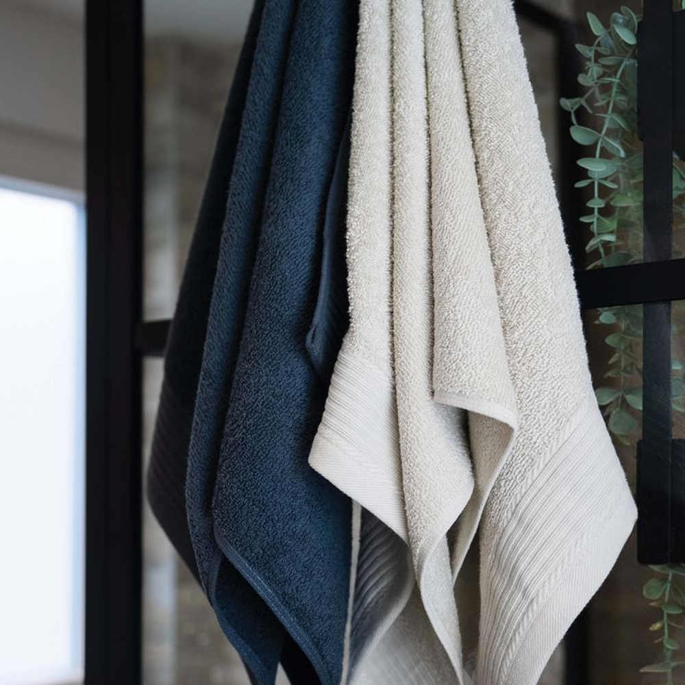 Three classic towels in navy, charcoal and beige hanging in a bathroom