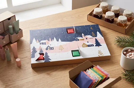 Printed advent calendar with chocolates, next to a beauty advent calendar, mini jam jars and tea bags