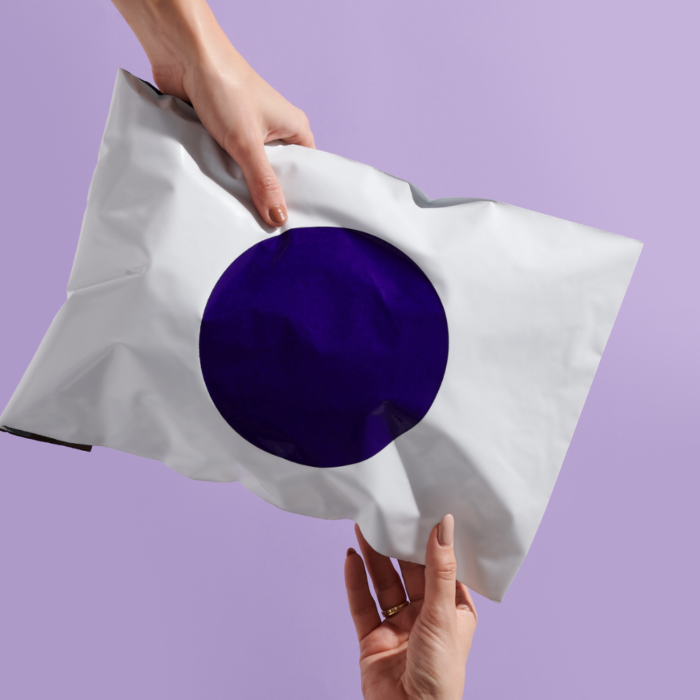 Mani che tengono un sacchetto postale riciclato bianco con cerchio viola stampato su sfondo lilla