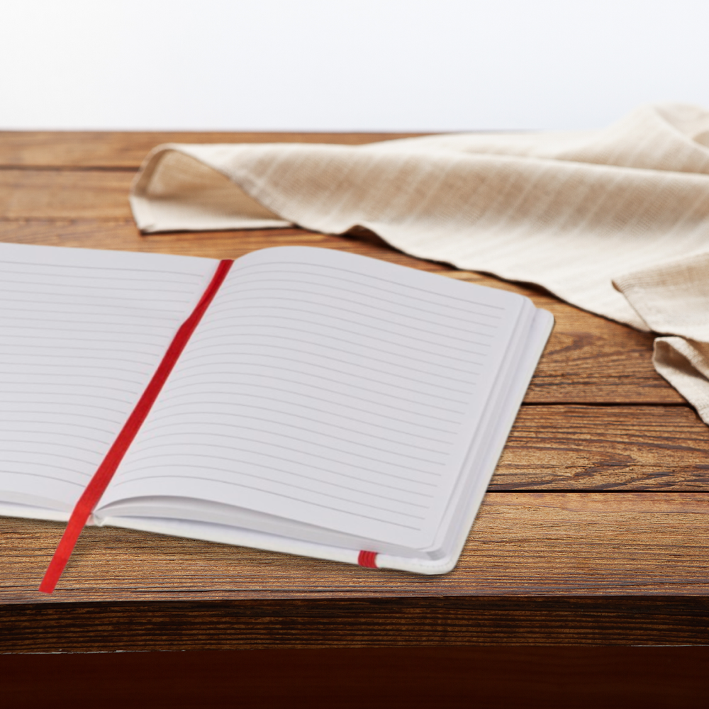 Open white A5 notebook with red strap and ribbon on a wooden desk