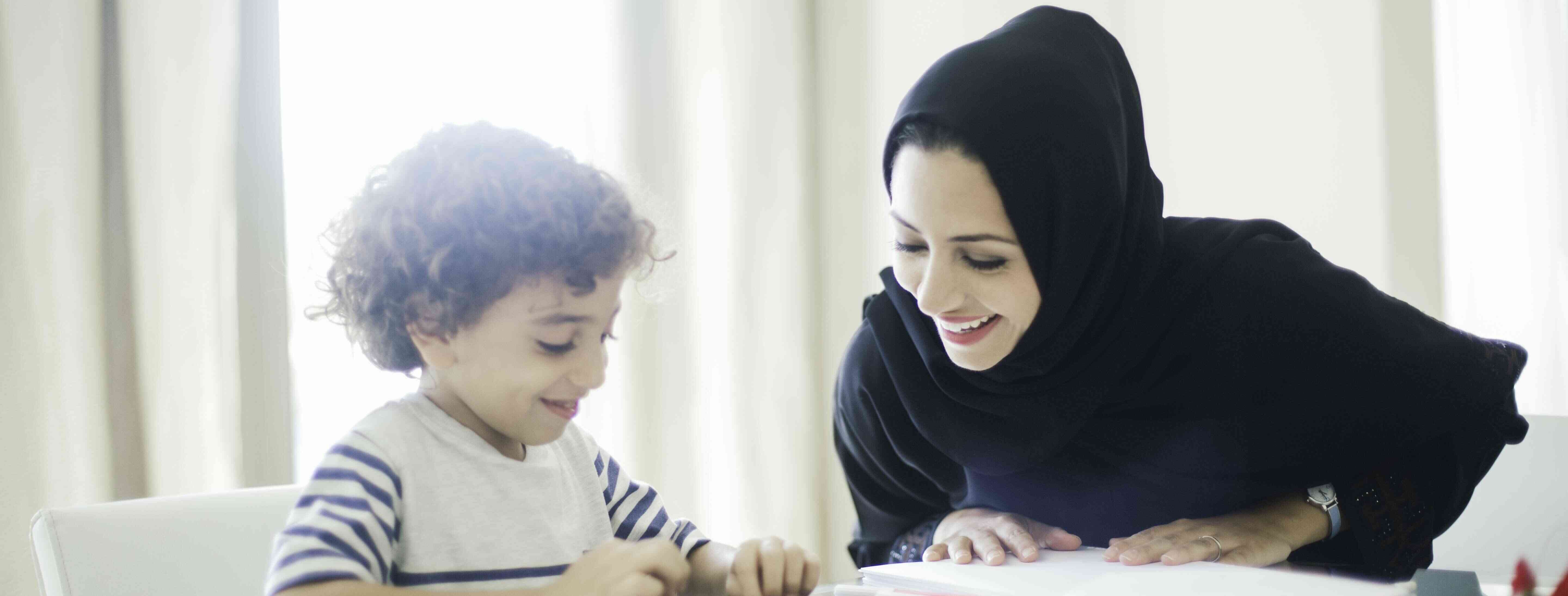 Bilingual babysitter in a hijab helping a child with a project