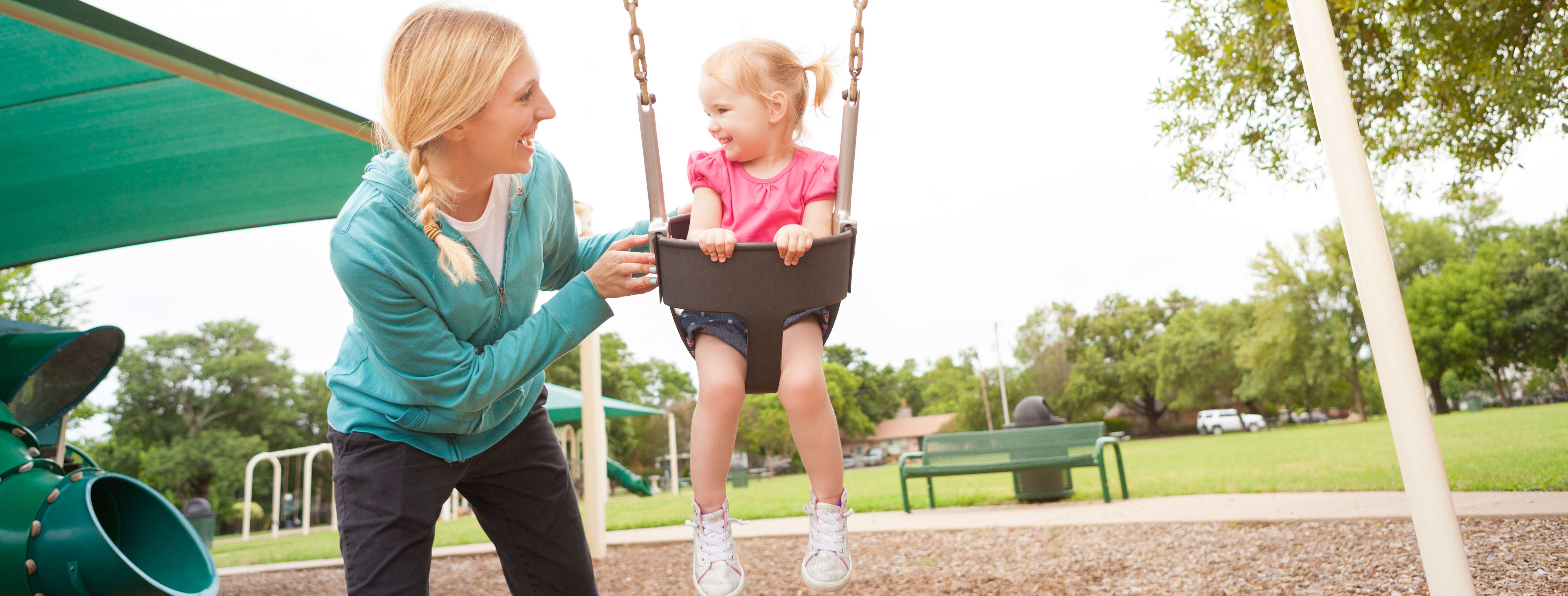 child care provider playing with a toddler on a swing