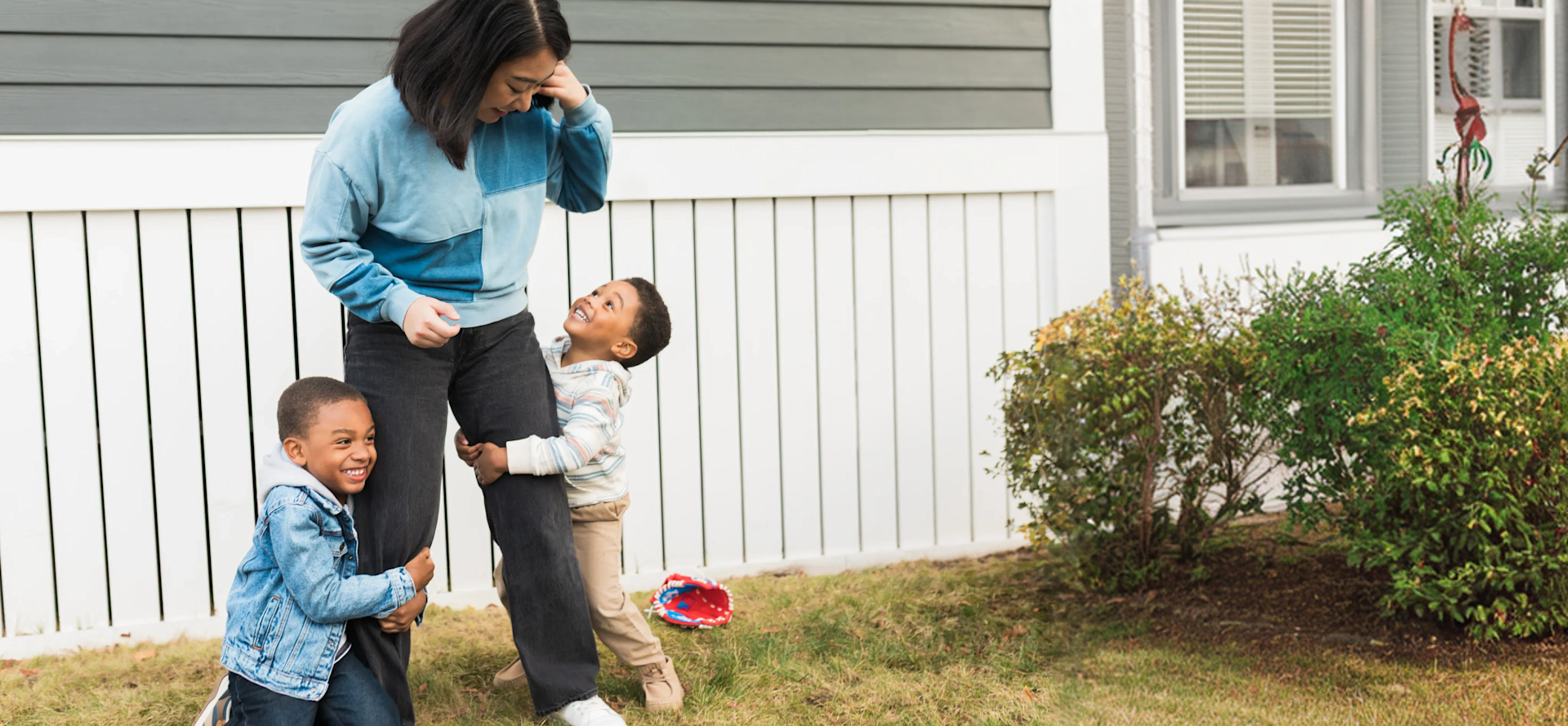 A caregiver with two smiling children in a sunny yard