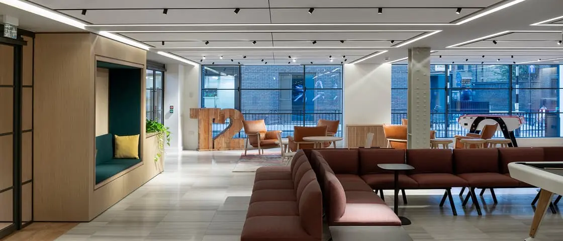 Modern office lounge with brown seating, wooden accents, and large windows providing natural light in a minimalist space.