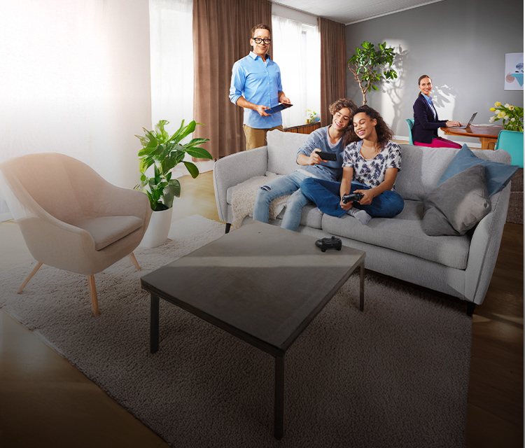 Personer i ett ljust vardagsrum med gröna växter. Två sitter i soffa med telefon, en står med surfplatta och en arbetar vid bord.