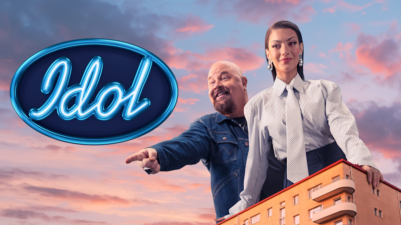 Två personer står på en byggnad med Idol-logotypen mot en solnedgångshimmel i rosa och blå toner.