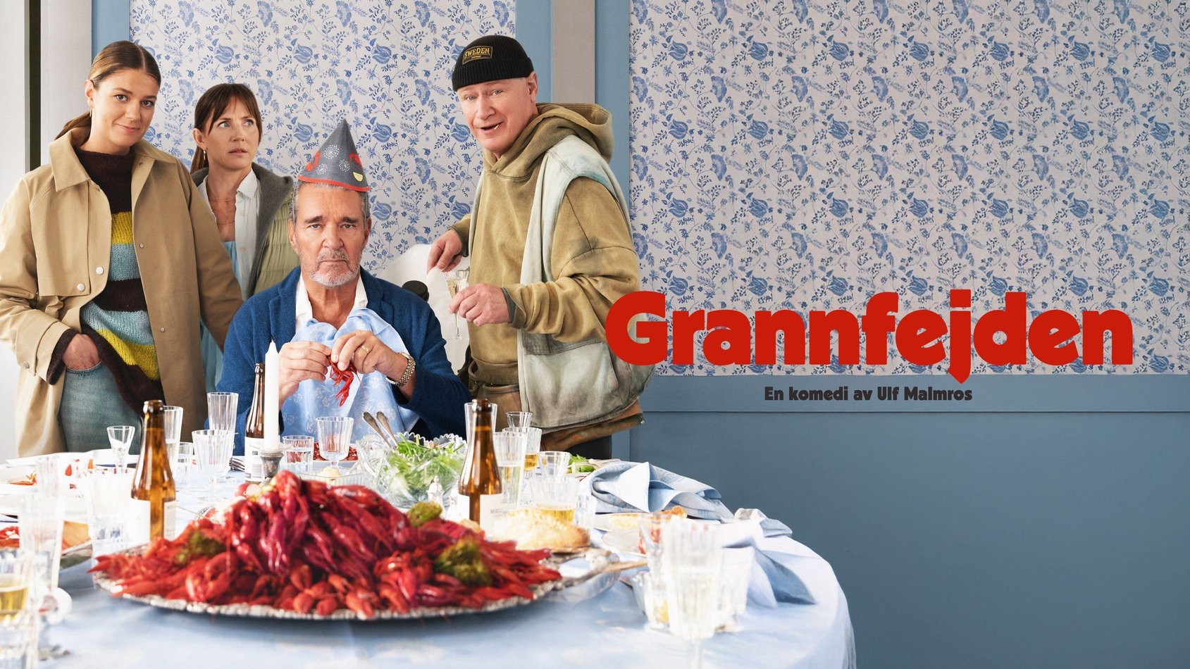 Fyra personer vid ett kräftskivabord. En man med pappersmössa sitter, omgiven av två kvinnor och en man i munkjacka.