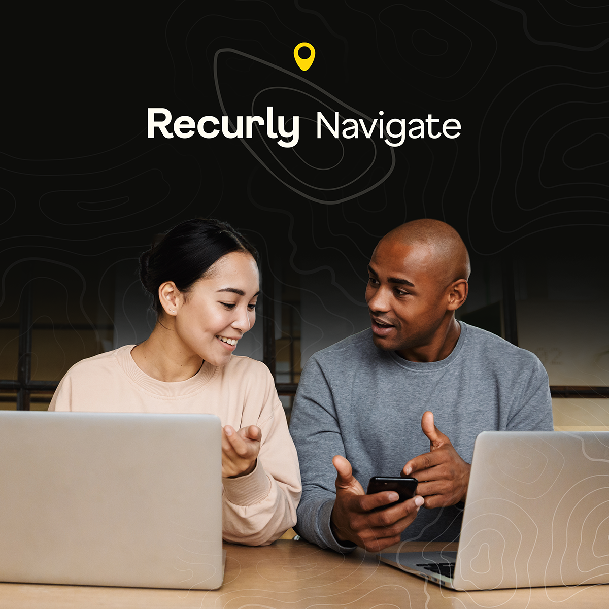 Two people, a woman and a man, smile and engage in conversation while using laptops and a smartphone.