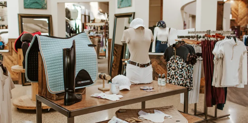 Equestrian apparel store display with riding boots, saddle pad, gloves, mannequins in riding outfits, and racks of clothing.