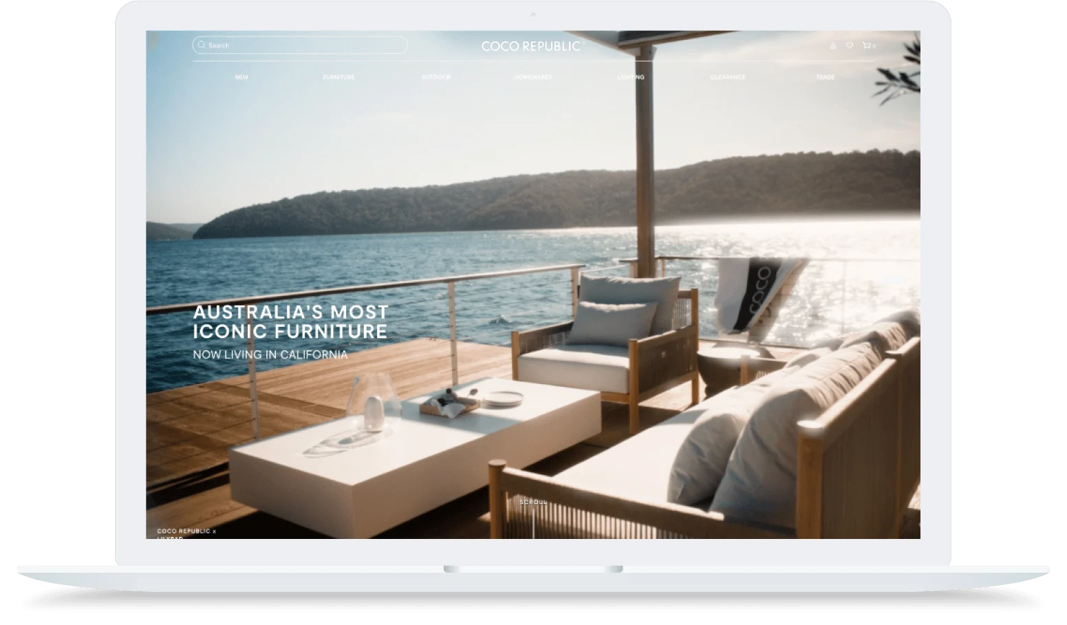 Outdoor lounge furniture on a sunny deck overlooking blue water and green hills, with modern white and wood accents.