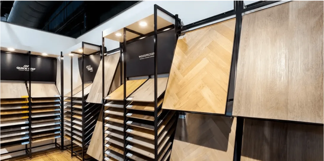 Display racks with various wood flooring samples in different shades and patterns under bright showroom lighting.