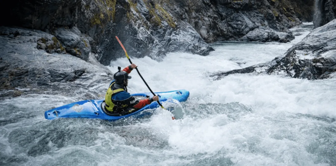 Kayaker in blue kayak paddles through whitewater rapids in a rocky river canyon.