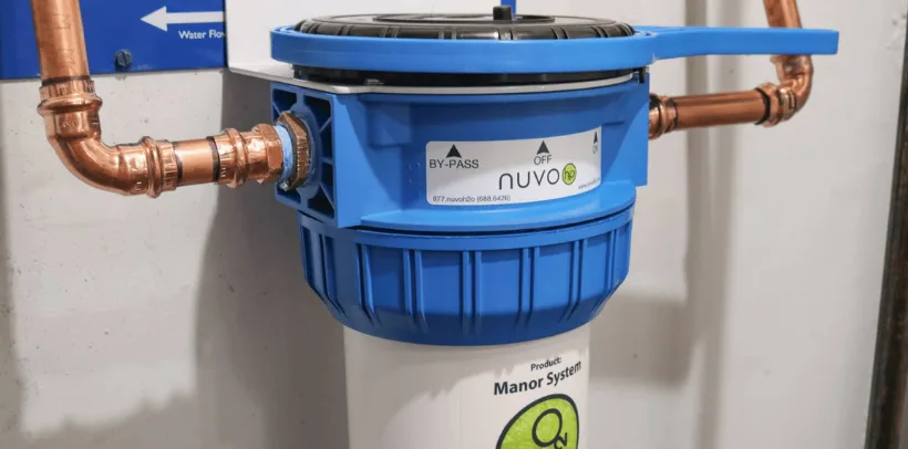 Blue NuvoH2O water filtration system with copper pipes mounted on a wall, labeled with by-pass and off settings.
