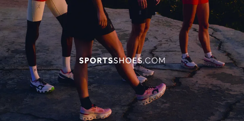 Four people in athletic wear stand outdoors on a rocky surface, showing off colorful running shoes at sunset.