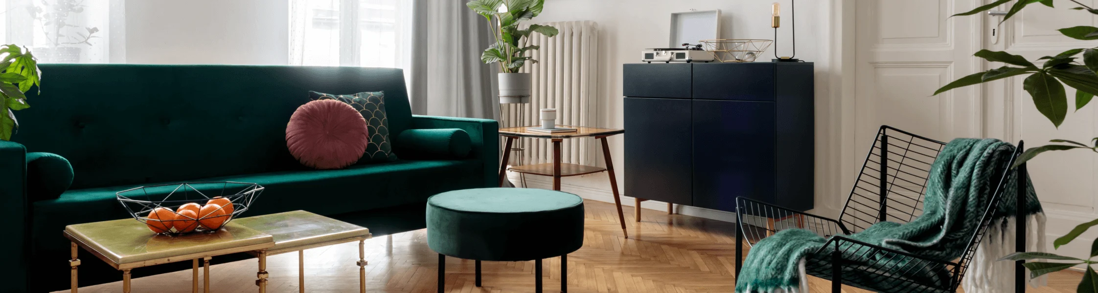 Stylish living room featuring a dark green velvet couch, matching ottoman, black console, and mid-century modern furniture on a hardwood floor.