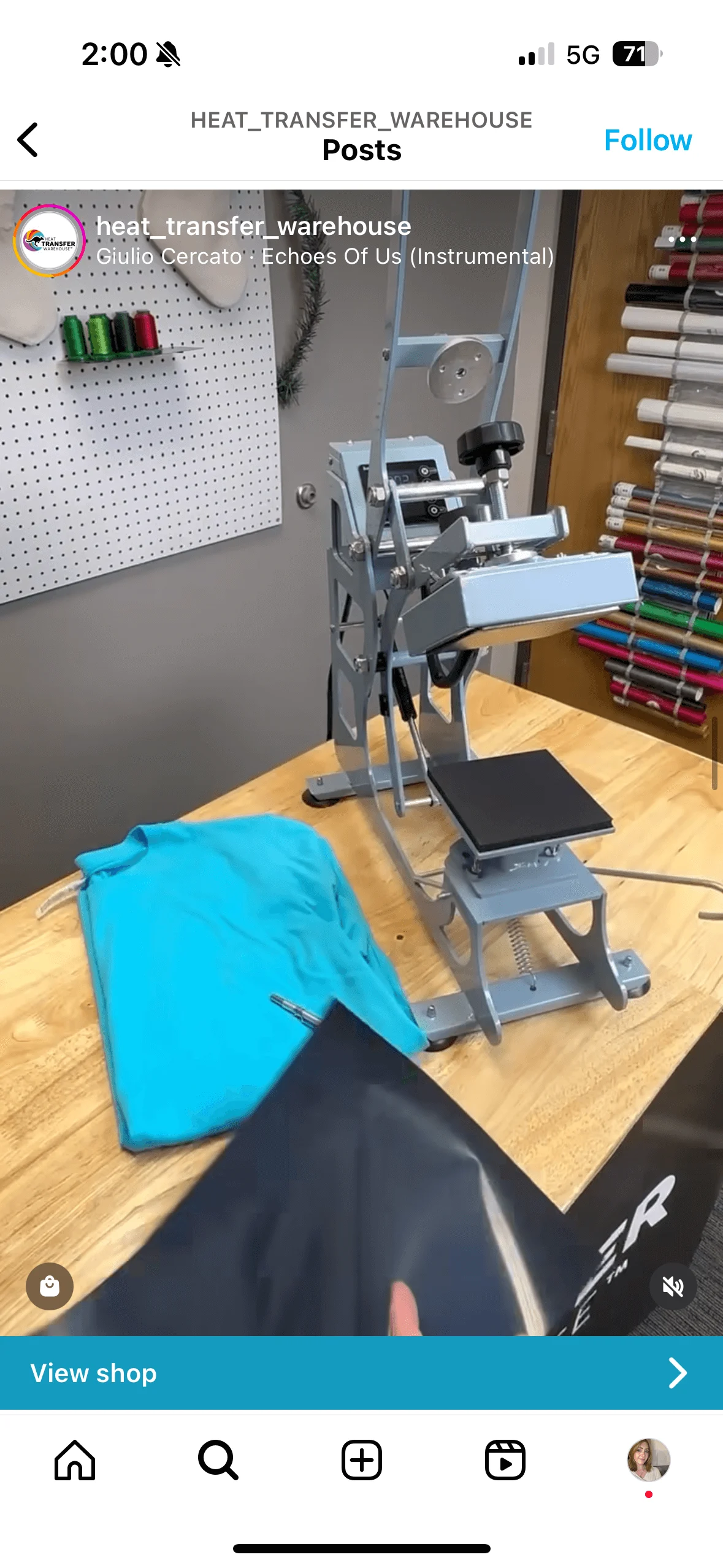 A heat press machine on a wooden table with a folded blue t-shirt and a hand holding black transfer vinyl.