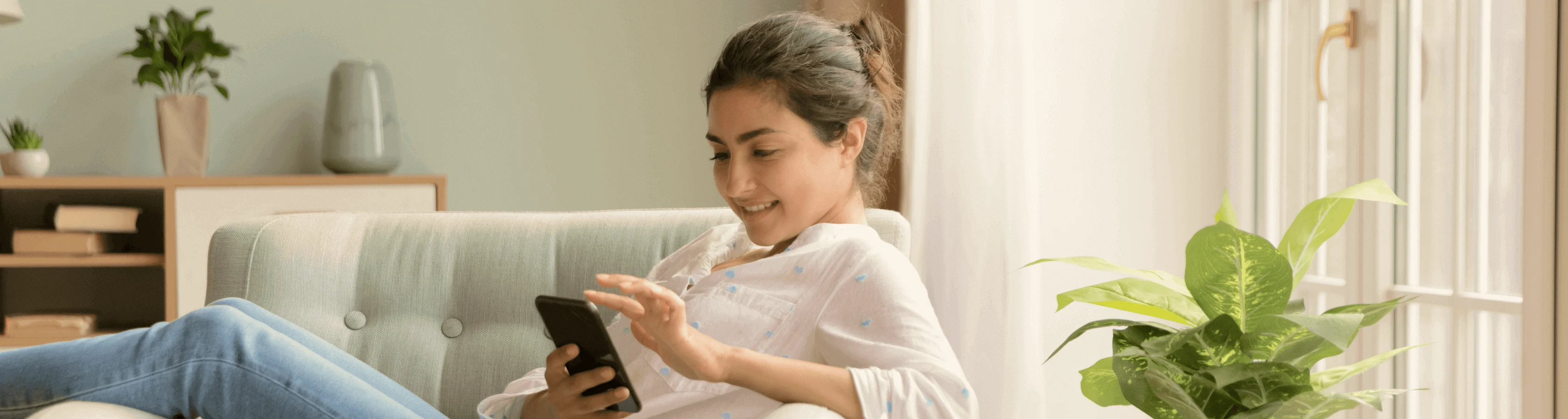 Smiling woman relaxing on a sofa and scrolling through content on her smartphone indoors.