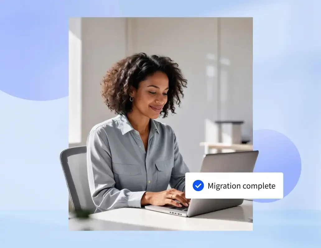 Smiling woman working on a laptop with a "Migration complete" notification overlay.
