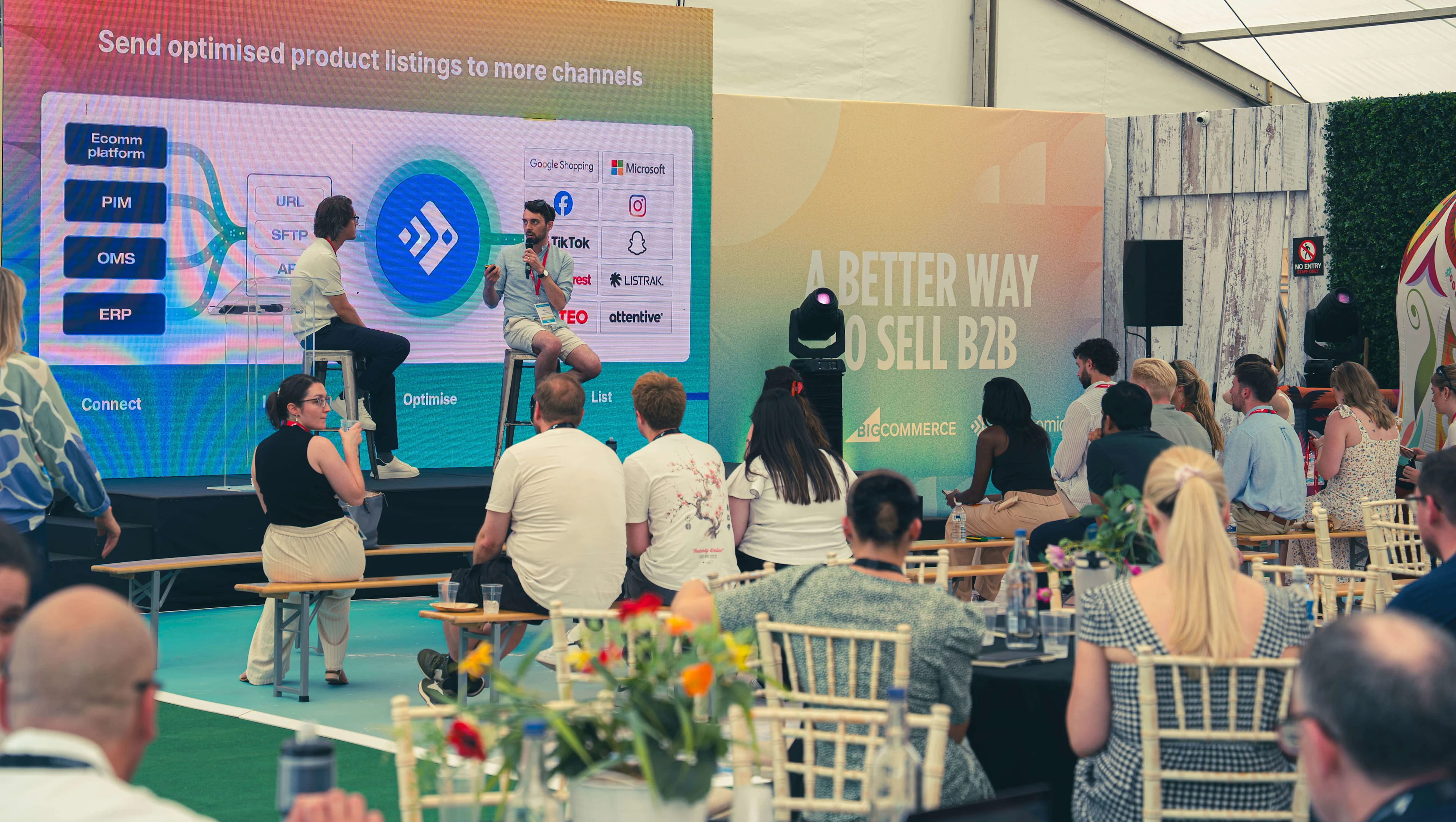 A speaker presents a BigCommerce slide on optimizing product listings to an audience at a live B2B sales event.