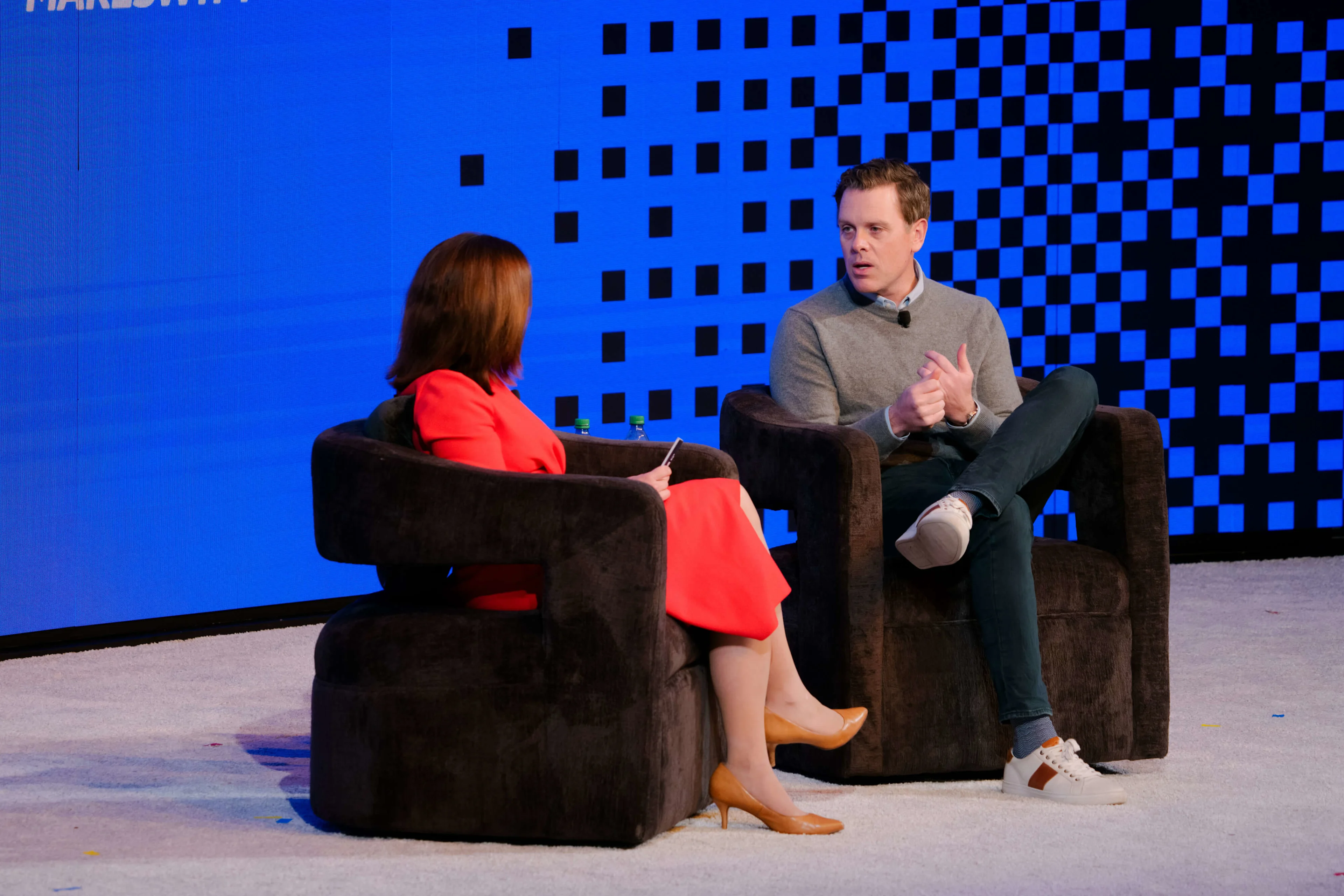 Michaela Weber, VP of Product Payments at Commerce and Mike Edmonds, VP of Agentic for Commercial Growth at PayPal . Two speakers in armchairs on stage, woman in red interviewing man in gray, against blue pixelated backdrop